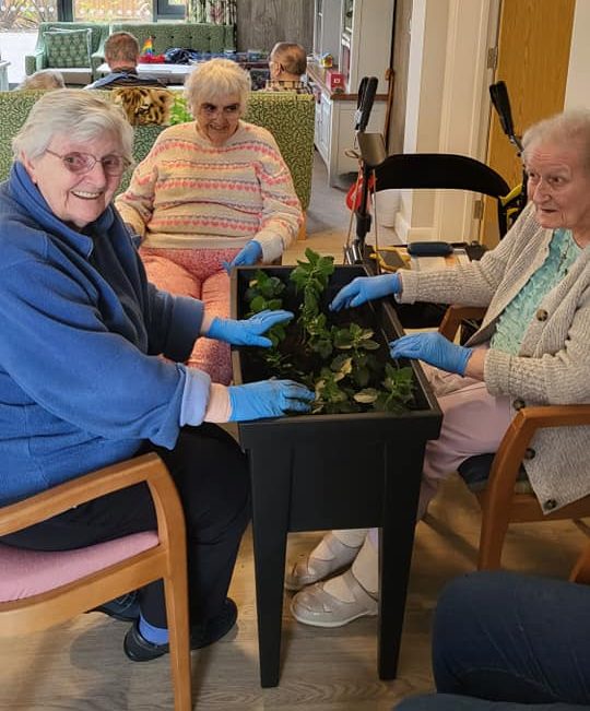 Residents planting flowers together during a Gardening Club activity at Richard House Care Home